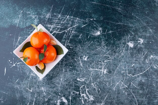 Geheel oranje fruit met groene bladeren op een witte plaat.