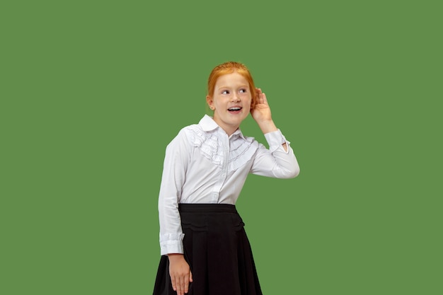 Geheim, roddelconcept. Jong meisje dat een geheim achter haar hand fluistert. Ze geïsoleerd op trendy groene studio achtergrond. Jonge emotionele tiener.