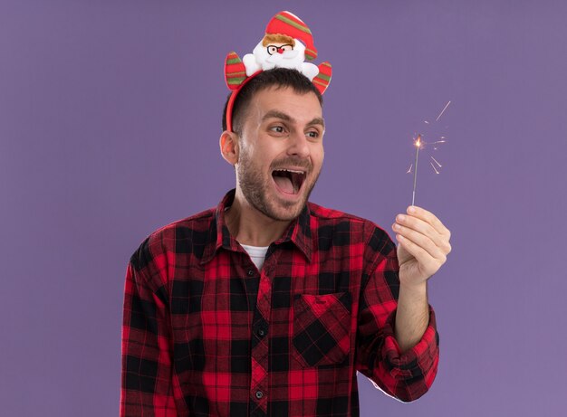 Geïmponeerde jonge blanke man met de hoofdband van de kerstman en kijkt naar vakantie sterretje geïsoleerd op paarse muur