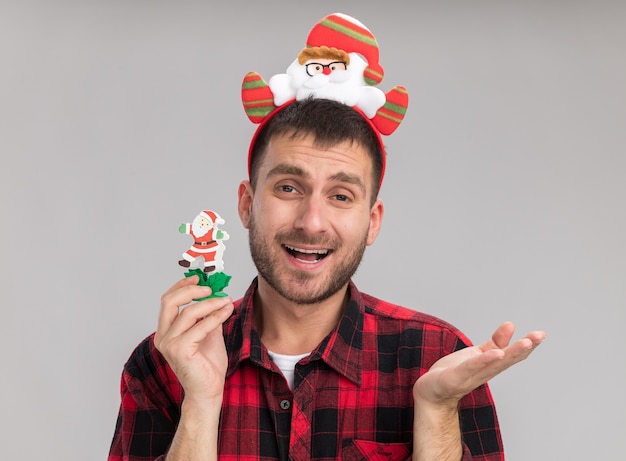 Geïmponeerde jonge blanke man met de hoofdband van de kerstman met sneeuwpop kerst speelgoed kijken naar camera met lege hand geïsoleerd op een witte achtergrond