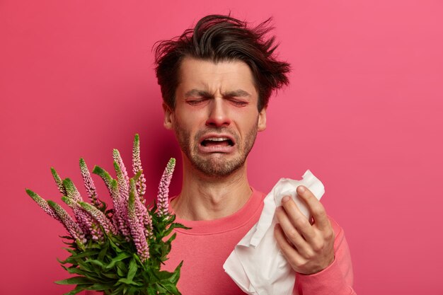 Geïnfecteerde man snuit neus in weefsel, heeft allergiesymptomen in de lente, kan niet goed ademen, niest constant, houdt de plant vast, huilt en voelt zich moe van de behandeling. Immunotherapie concept