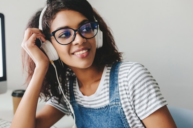 Gratis foto geïnspireerd brunette meisje met een gebruinde huid lachen tijdens het luisteren naar muziek op kantoor