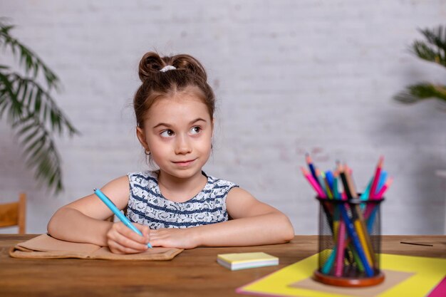 Geïnspireerd meisje aan tafel tekenen met kleurpotloden of huiswerk maken. Studeren op de basisschool. Thuisonderwijs