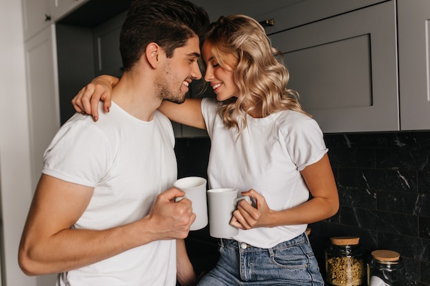 Geïnspireerd meisje dat van ochtend met echtgenoot geniet. indoor portret van koelende paar koffie drinken.