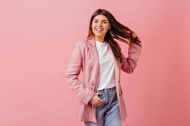 Geïnspireerde dame die met haar speelt en lacht. Studio shot van meisje in casual kleding geïsoleerd op roze achtergrond.