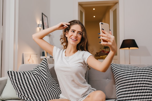 Geïnspireerde jonge vrouw die in een gezellige kamer zit en een foto van zichzelf neemt