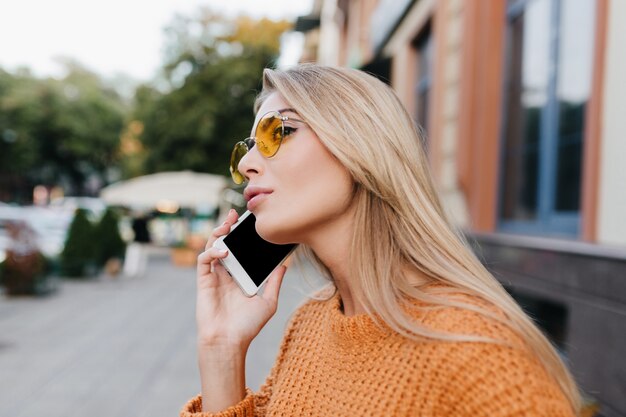 Geïnspireerde vrouw met lang blond haar die iemand belt en in de verte kijkt