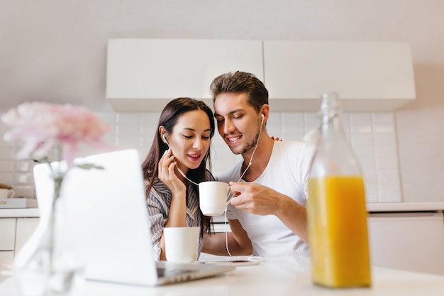 Geïnteresseerd vrouwelijk model in witte oortelefoons lachen met echtgenoot tijdens gezamenlijke lunch
