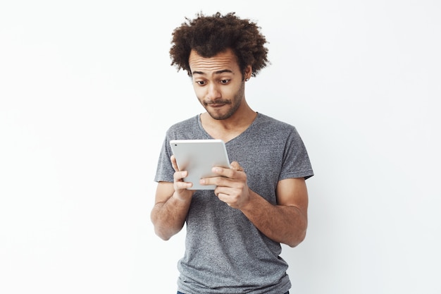 Geïnteresseerde Afrikaanse mens die tablet over witte bakground bekijken.