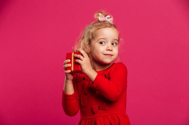 Geïntrigeerd jong blondemeisje in de giftdoos van de rode kledingsholding