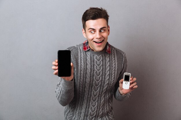 Geïntrigeerde man in trui kiezen tussen smartphones en kijken