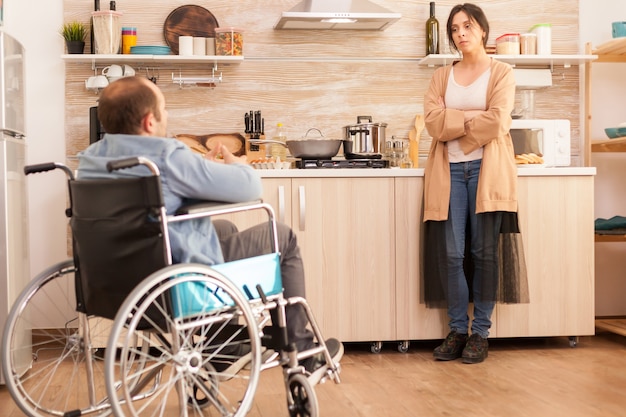 Gratis foto geïrriteerde vrouw in keuken vanwege onenigheid met gehandicapte man in rolstoel. gehandicapte verlamde gehandicapte man met loopbeperking integreren na een ongeval.