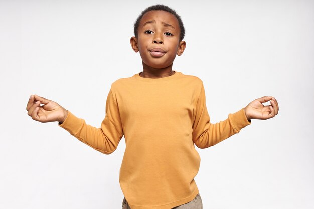 Geïsoleerd Portret van emotionele grappige donkere huid kleine jongen hand in hand in mudra gebaar, uitademen, ademhalingsoefeningen doen om te kalmeren