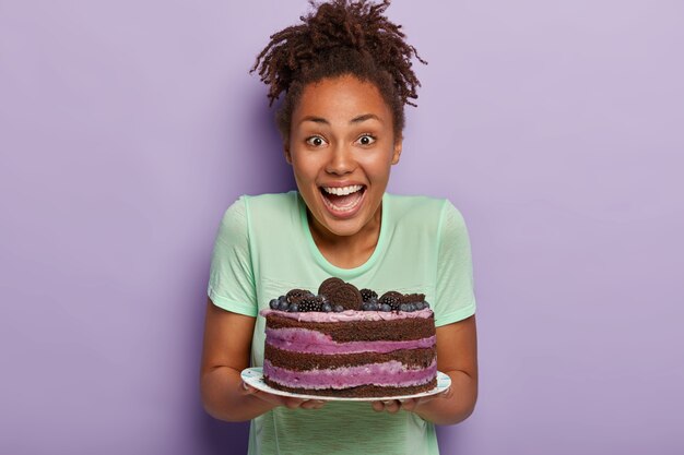 Geïsoleerde schot van dolblij Afro huisvrouw blij om heerlijke bosbessencake te bakken