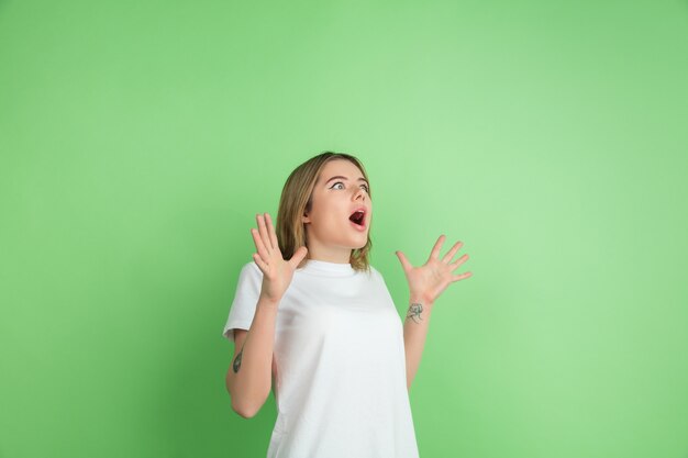 Gek geschokt. Portret van de blanke jonge vrouw geïsoleerd op groene studio muur.