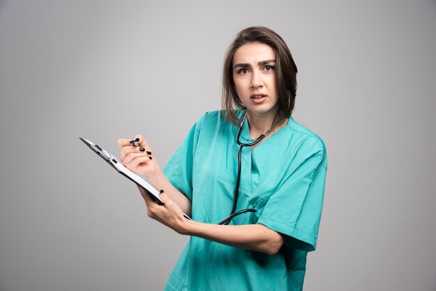 Gekke dokter in blauwe uniform staande op grijze muur.