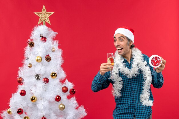 Gekke emotionele jonge man met kerstman hoed en met een glas wijn en klok