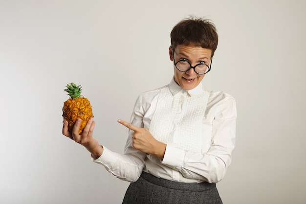 Gekke leraar maakt grappig gezicht wijzend op een ananas in haar hand op een witte muur