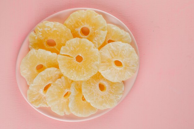 Gekonfijte ananas ringen in een plaat op een roze oppervlak