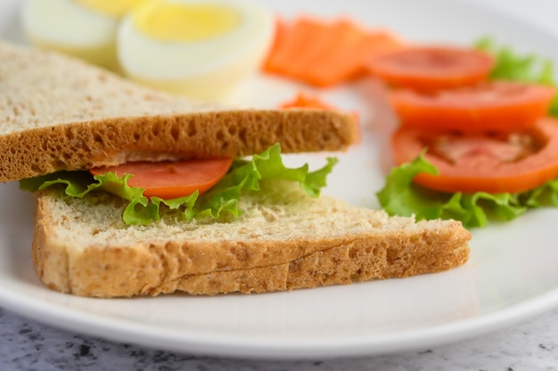 Gekookte eieren, brood, wortelen en tomaten op een witte plaat met een mes en vork.