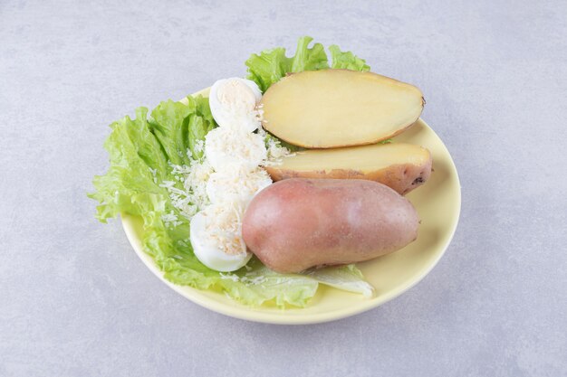 Gekookte eieren en aardappelen op gele plaat.