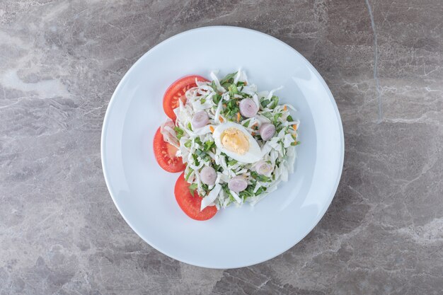 Gekookte eieren met groentesalade op witte plaat.