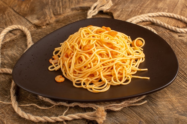gekookte Italiaanse pasta met garnalen in bruine plaat met touwen op houten bureau