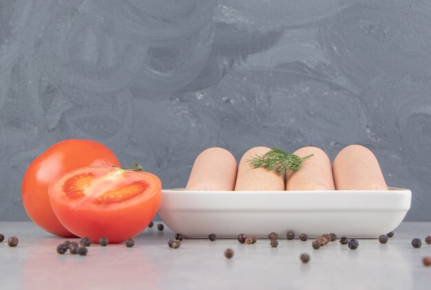 Gekookte smakelijke worstjes op wit bord met tomaten.