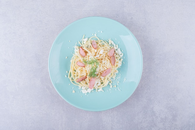 Gekookte spaghetti met gesneden worstjes op blauw bord.