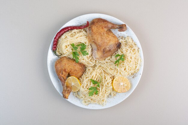 Gekookte spaghetti, peper en kippenbenen op witte plaat