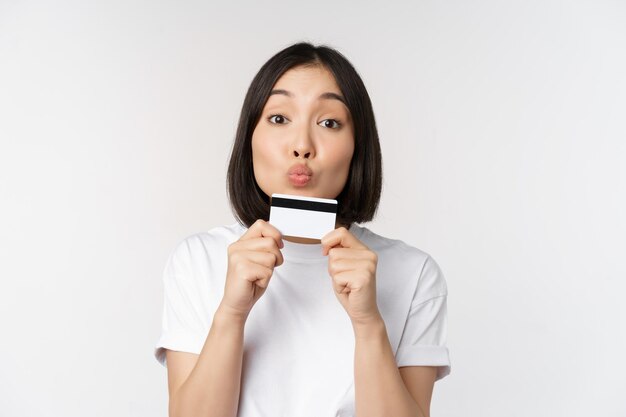 Geld en financiënconcept Leuk Japans meisje dat haar creditcard kust die zich in t-shirt over witte achtergrond bevinden