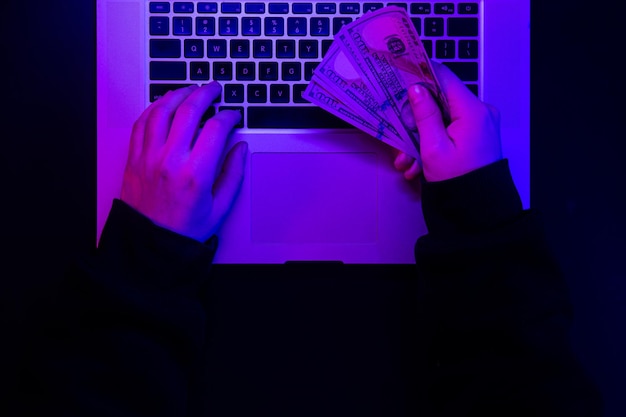 Geld in mannelijke handen op de achtergrond van een laptoptoetsenbord in neonverlichting