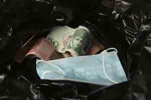Gratis foto geld van over de hele wereld en een gezichtsmasker in een zwarte plastic vuilniszak.