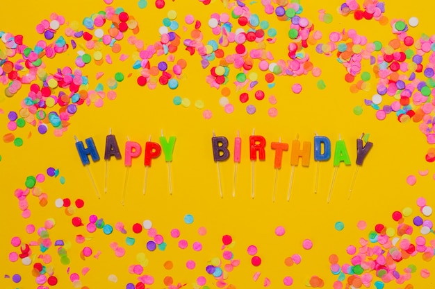 Gele achtergrond met confetti en de letters &quot;happy birthday&quot;