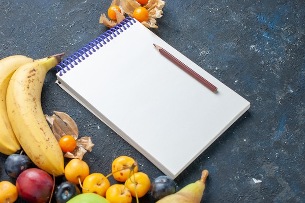 Gele bananen met verse groene appels peren pruimen blocnote en zoete kersen op donker