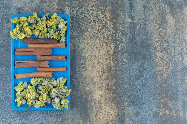 Gratis foto gele bloemen en kaneelstokjes op blauw bord.