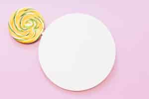 Gratis foto gele en groene gestreepte lolly over het witte cirkelkader tegen roze achtergrond
