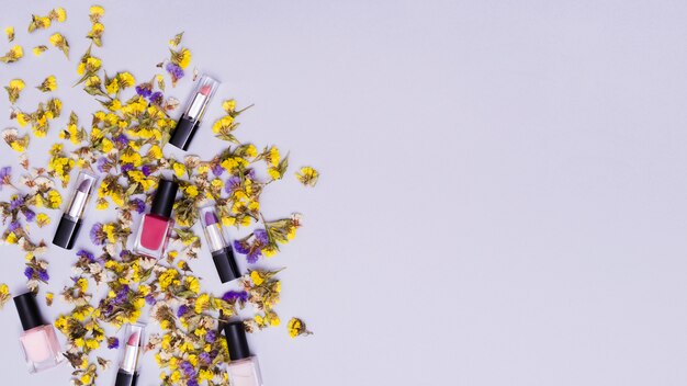 Gele en purpere bloemen met kleurrijke lippenstiften en roze spijkervernis op gekleurde achtergrond