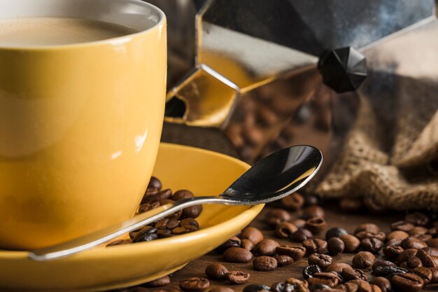 Gele koffie die dichtbij bonen en geiserkoffiezetapparaat wordt geplaatst