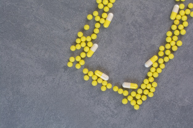 Gele medische tabletten en capsules op marmeren tafel.