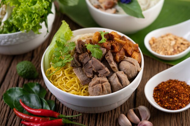 Gele noedels in een kopje met knapperig varkensvlees, plakjes varkensvlees en gehaktballen samen met Thaise noedels in voedselstijl