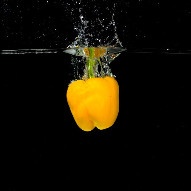 Gele paprika spatten in het water tegen zwarte achtergrond
