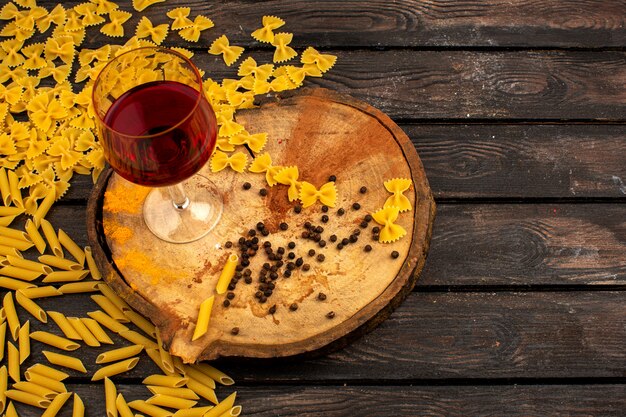 Gele pasta rauw samen met peper en fles wijn op een ronde houten bureau op een bruine tafel