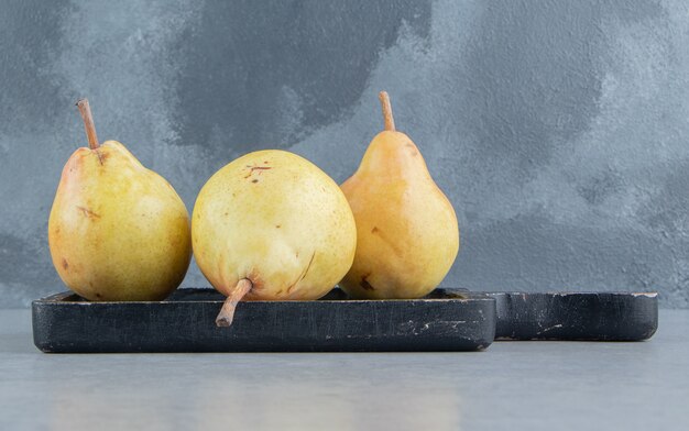 Gele peren op een zwart bord op marmer.