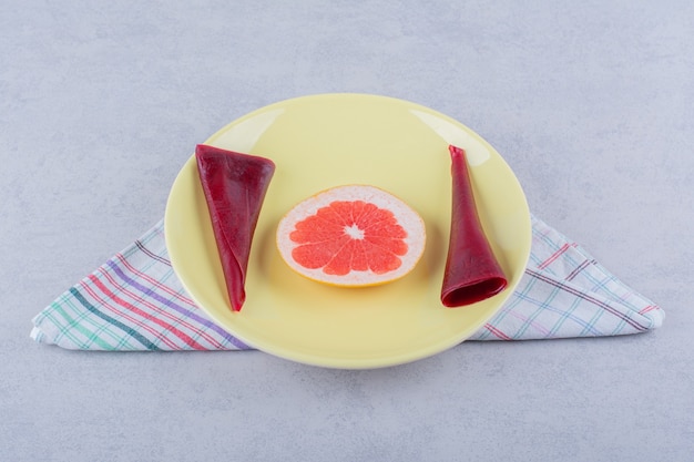 Gele plaat van droog fruitpulp en grapefruit op steen.