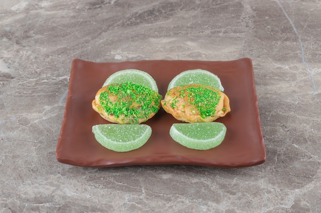 gelei-snoepjes en kleine broodjes met groene topping op een schotel op marmeren ondergrond