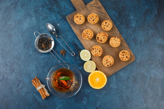 Gelei vullende taarten op een snijplank met een kopje thee, theezeefjes, kruiden en citrusvruchten