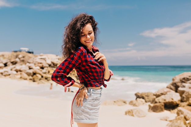 Gelooide vrij gelukkige vrouw, gekleed in geruite overhemd en denim shorts ontspannen op het eiland