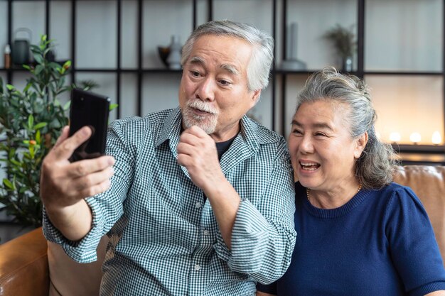 Geluk aziatisch oud senior gepensioneerd koppel geniet van videogesprek met familie samen op de bank in de woonkamer bij homeaziatische mensen gebruiken smartphonecommunicatie naar het concept van gezinsisolatie