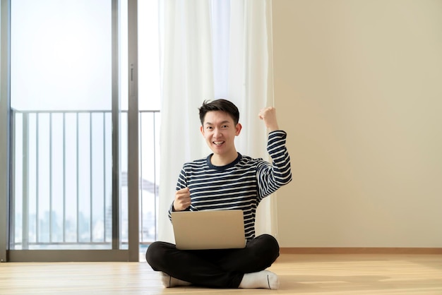 Geluk aziatische smart casual bril man werken vanuit huis met laptop technologie met comfortabele en ontspannen gezichtsuitdrukking modern huis met lege ruimte interieur achtergrond